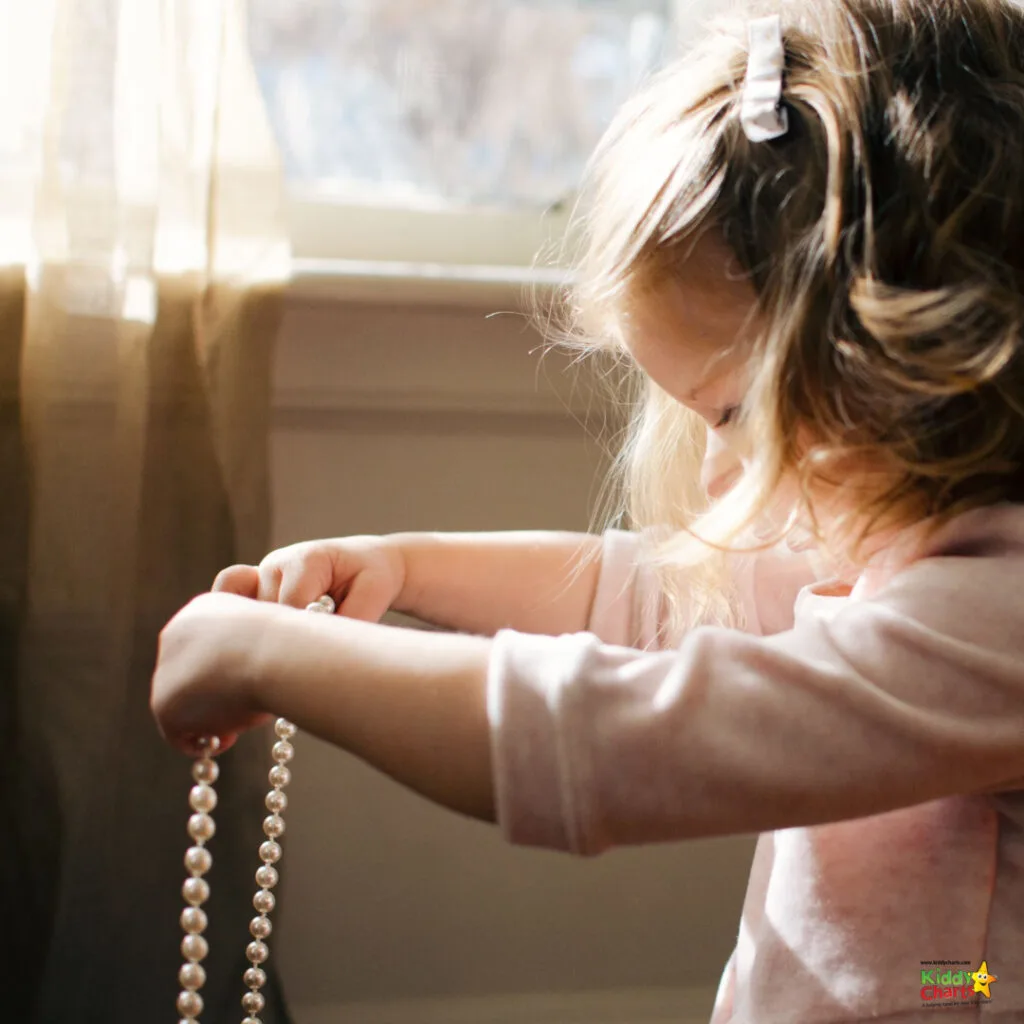A young child, bathed in natural light, is focused on threading beads onto a string. The warm setting creates a peaceful atmosphere.