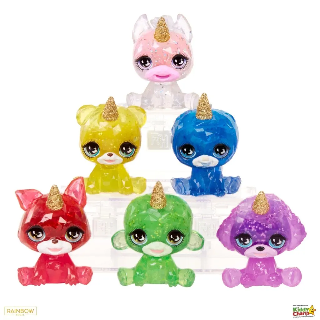The image shows a collection of six colorful, sparkly toy figures with oversized heads, large eyes, and unicorn horns, arranged in a pyramid formation.
