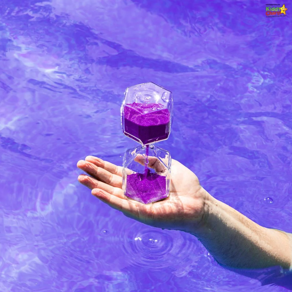 A person holds a transparent hourglass with purple sand over a vibrant purple water background, creating a striking visual contrast.