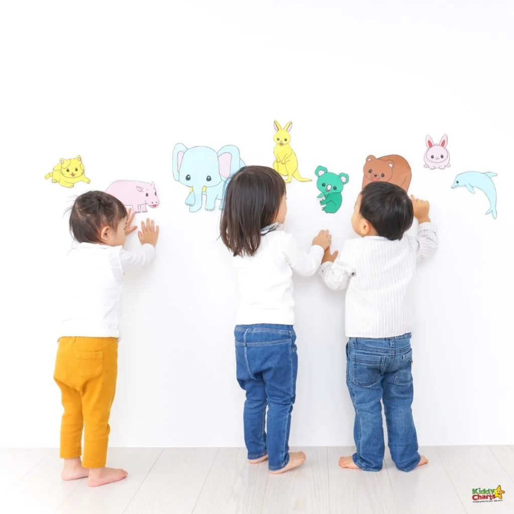 Three children interact with colorful animal cutouts on a white wall indoors, showcasing engaging and educational playtime in a bright setting.