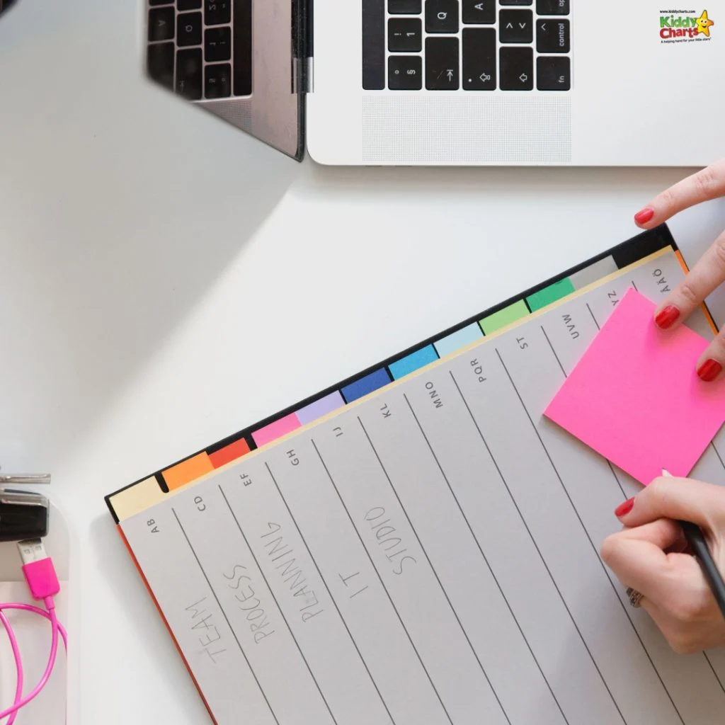 A person writes on a pink sticky note with a planner and laptop nearby on a white desk.