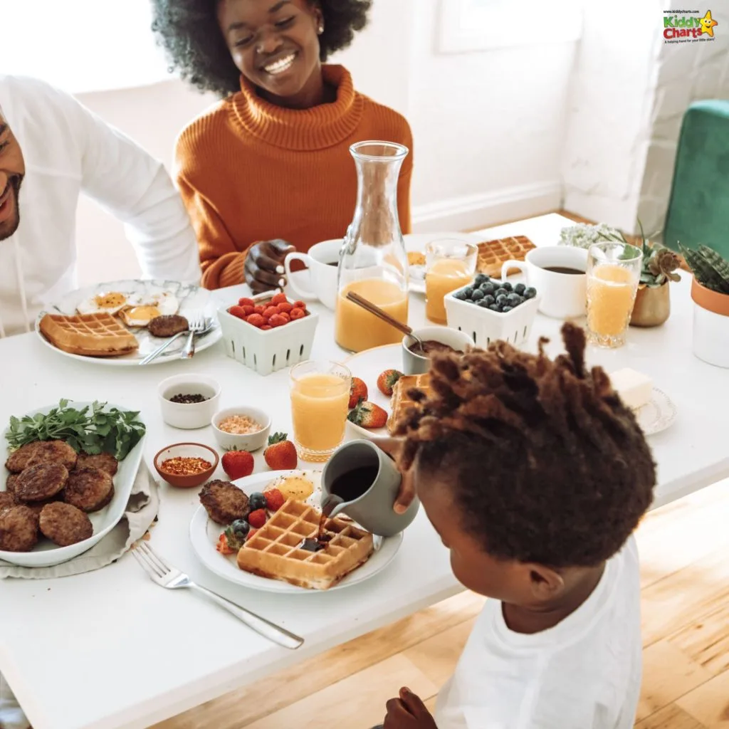 Three people enjoy a breakfast spread of waffles, fruit, and drinks at a bright, cozy table setting. One child pours syrup.