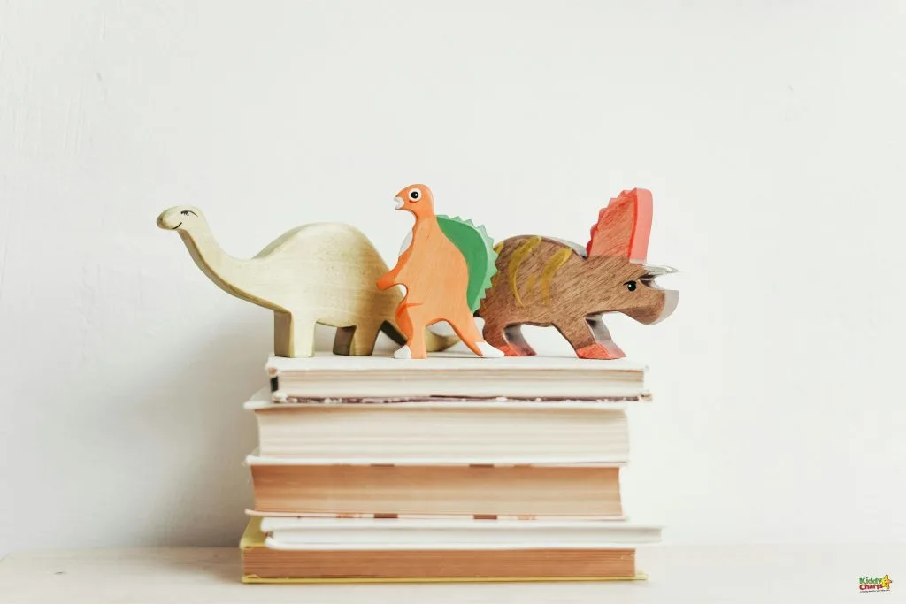 Three colorful wooden dinosaur toys are lined up on a stack of books against a plain white background.