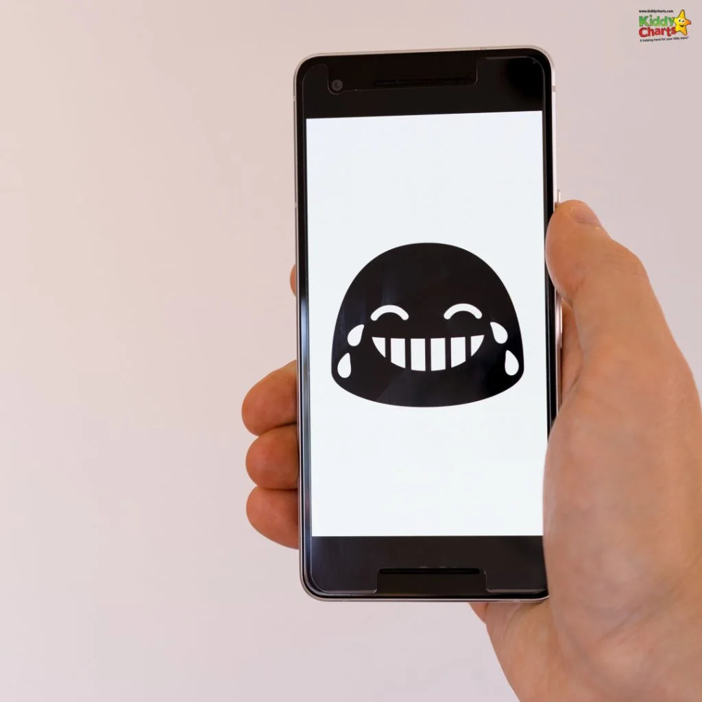 A person holds a smartphone displaying a laughing emoji with tears, against a plain background. The phone is gripped in one hand.