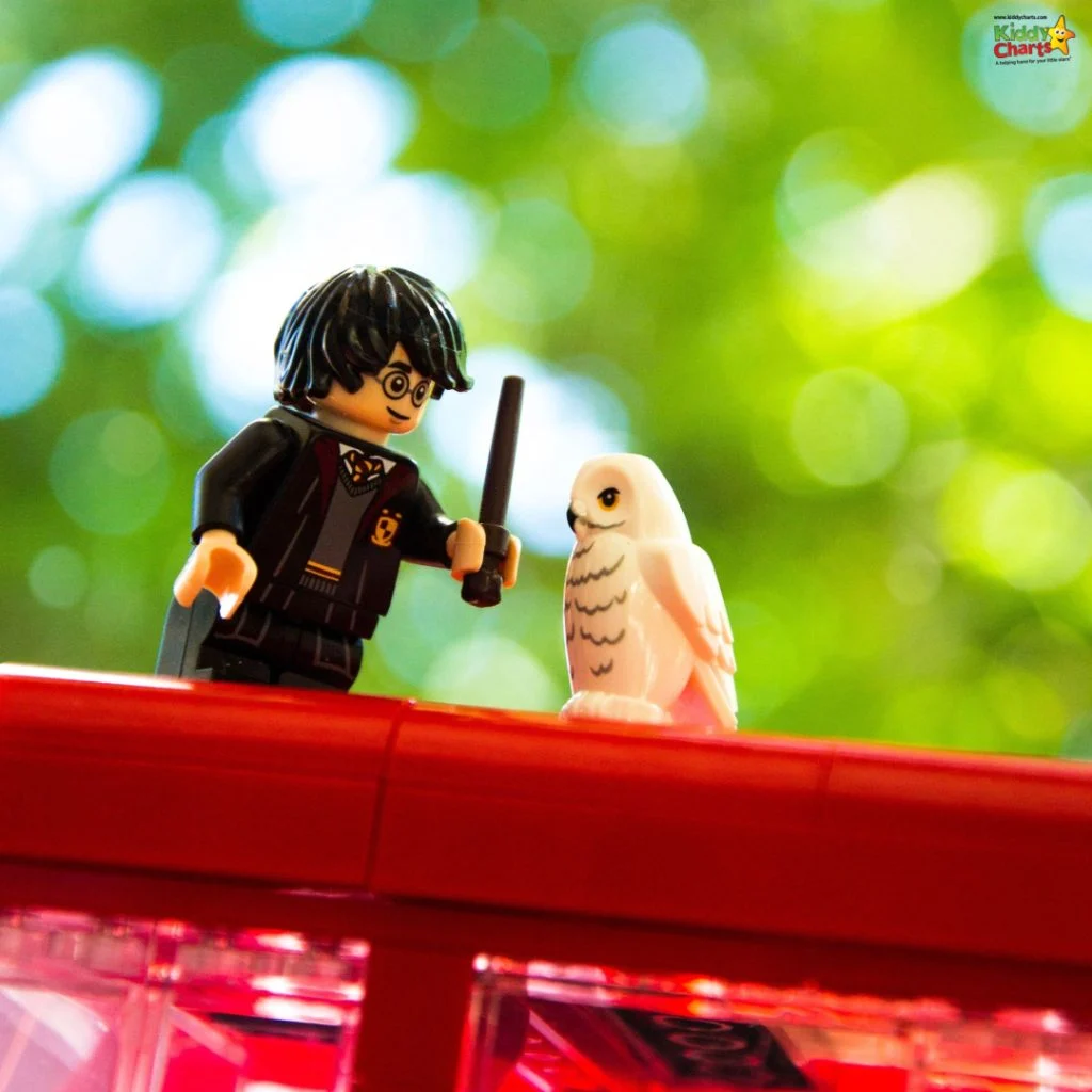 A LEGO figure with glasses and a wand stands beside a white owl on a red surface, set against a green bokeh background.