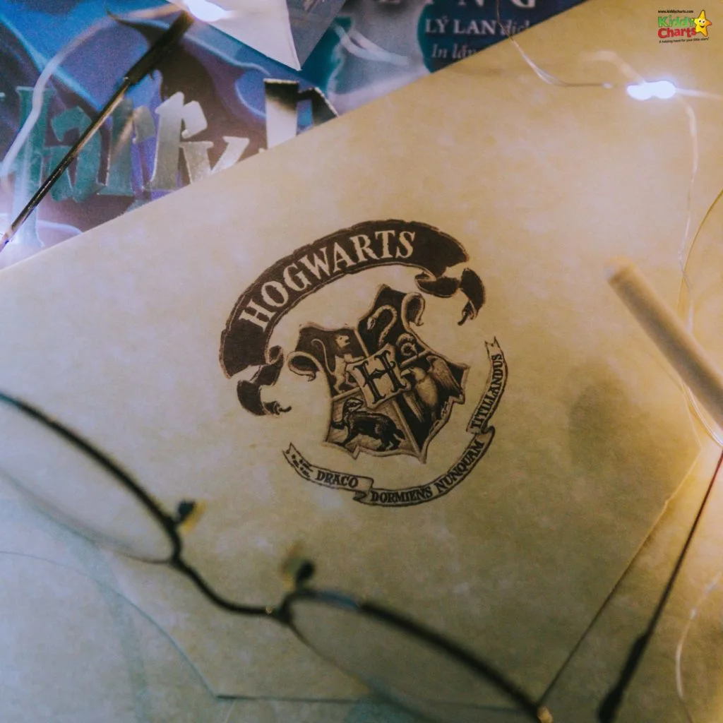 Envelope with the Hogwarts crest surrounded by fairy lights, glasses, and a Harry Potter book partially visible in the background.