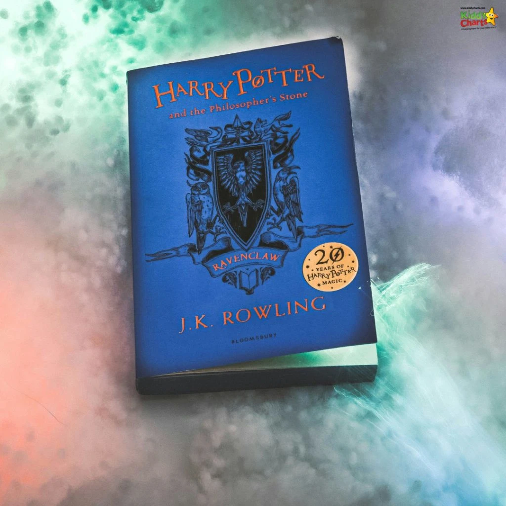 A "Harry Potter and the Philosopher's Stone" book with a Ravenclaw-themed cover, commemorating 20 years of magic, lays on a misty background.