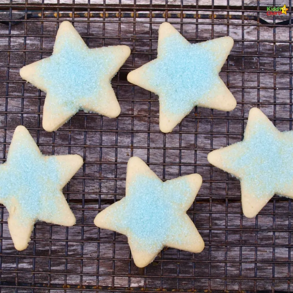 Five star-shaped cookies with light blue sugar coating are cooling on a wire rack over a wooden surface.