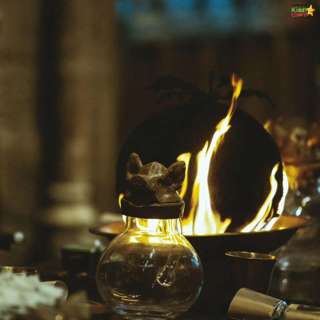 A decorative glass container with pig-shaped lid and burning fire behind, surrounded by ceremonial objects in a dimly lit setting.