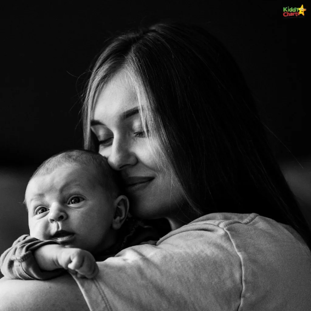 A black-and-white image of a person gently hugging a baby, both expressing contentment. KiddyCharts logo in the top corner.