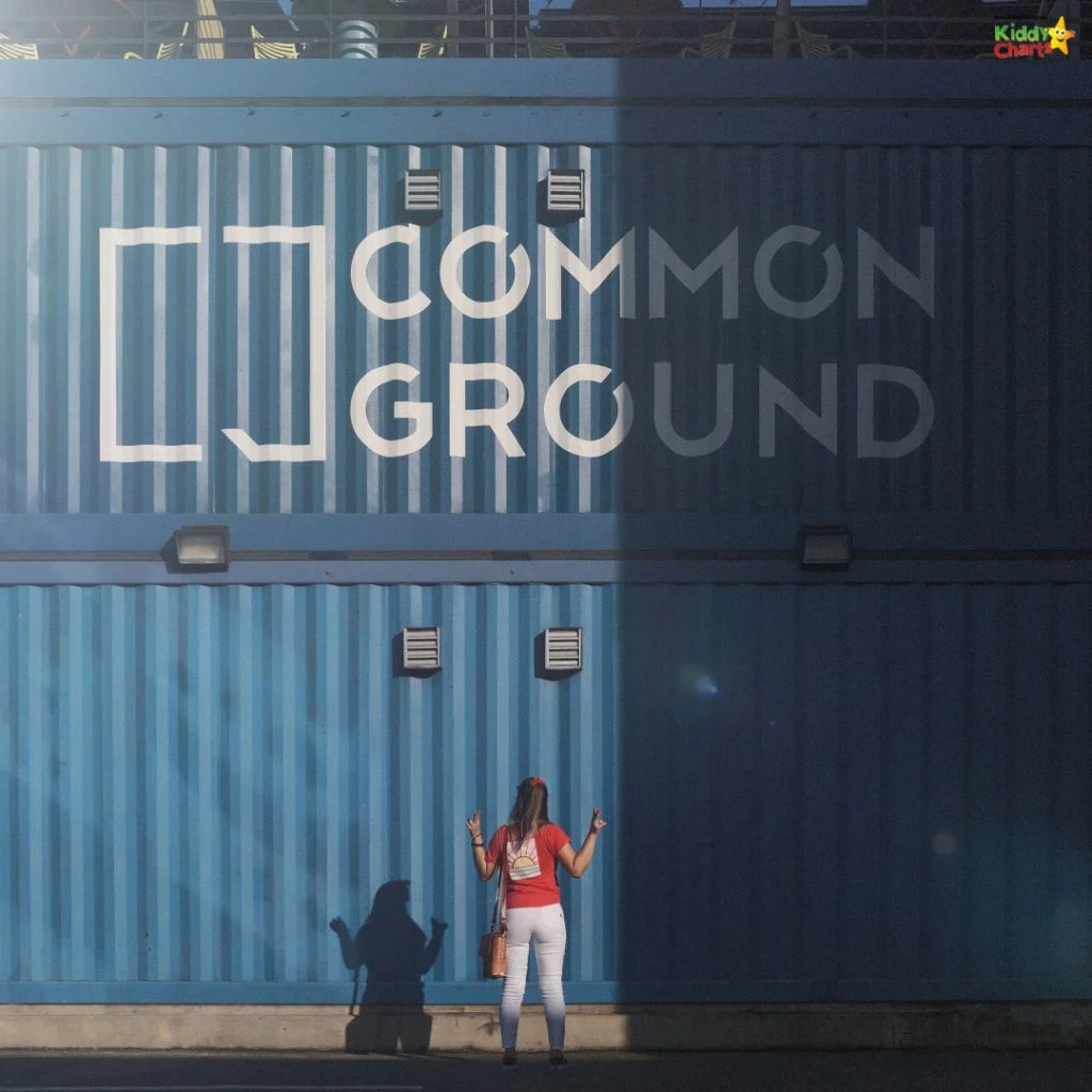 A person facing a blue building with "Common Ground" signage, standing with raised hands casting a shadow on the wall.