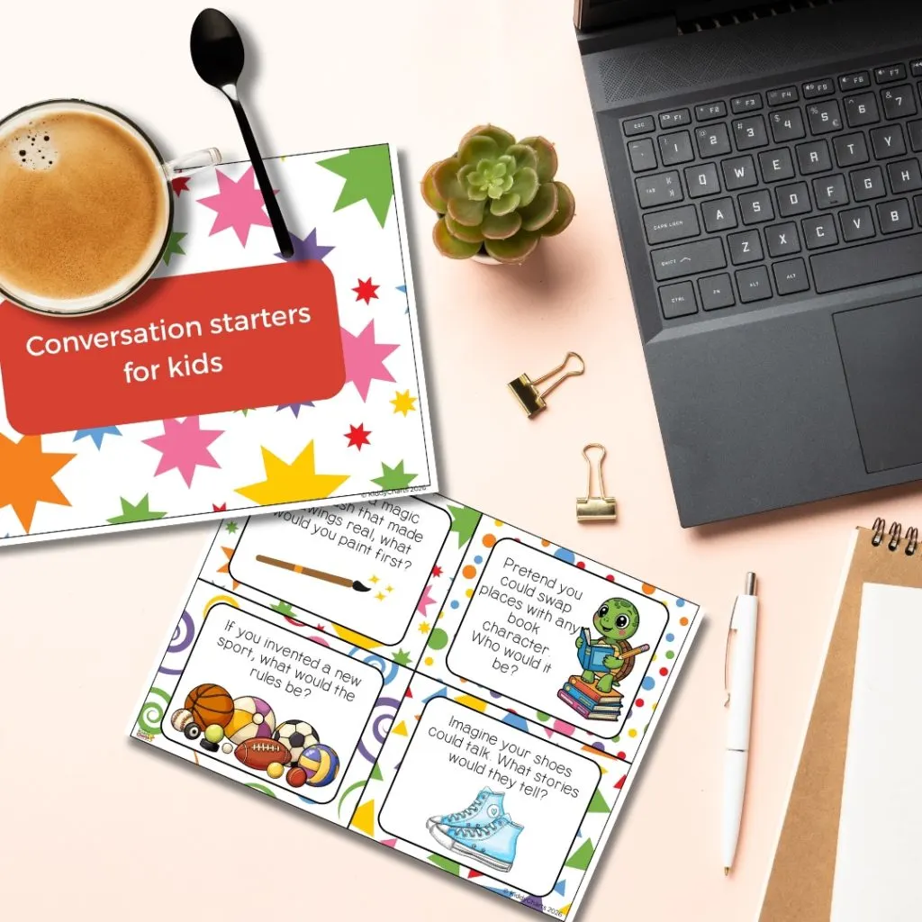 A laptop, coffee, succulent, and conversation starter cards for kids are arranged on a desk with colorful designs and various playful prompts.