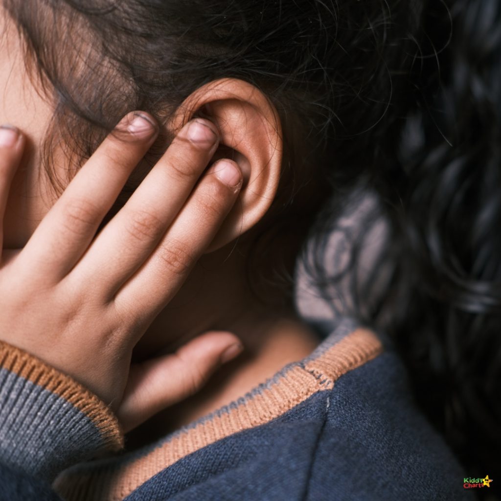 A child wearing a blue sweater touches their ear, with dark hair partially visible, captured in a close-up.