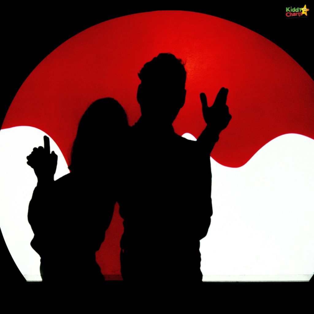 Two silhouetted people in front of a bright red and white abstract background, suggesting playful interaction. No recognizable landmarks present.