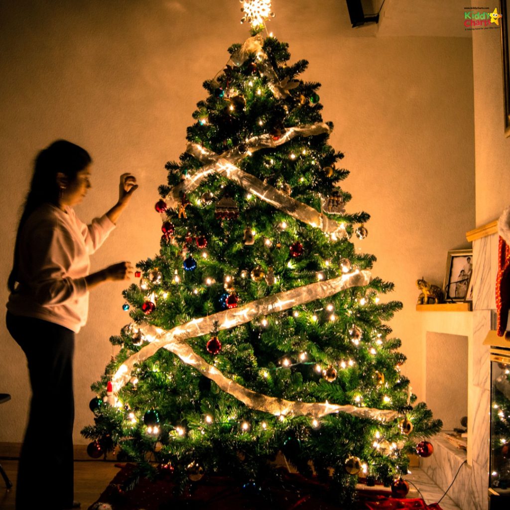 A person decorates a beautifully lit Christmas tree in a warmly lit room, creating a festive and cozy holiday atmosphere.
