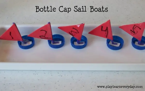 A group of carmine origami bottle cap sail boats are floating in a pool of water.