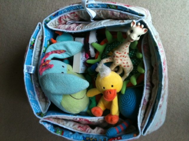 A handmade plush Easter toy sits amongst a variety of baby toys indoors.
