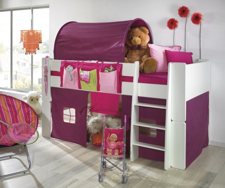 A person is decorating a nursery with a pink bed, magenta linens, purple furniture, and a red dollhouse, creating a vibrant interior design.