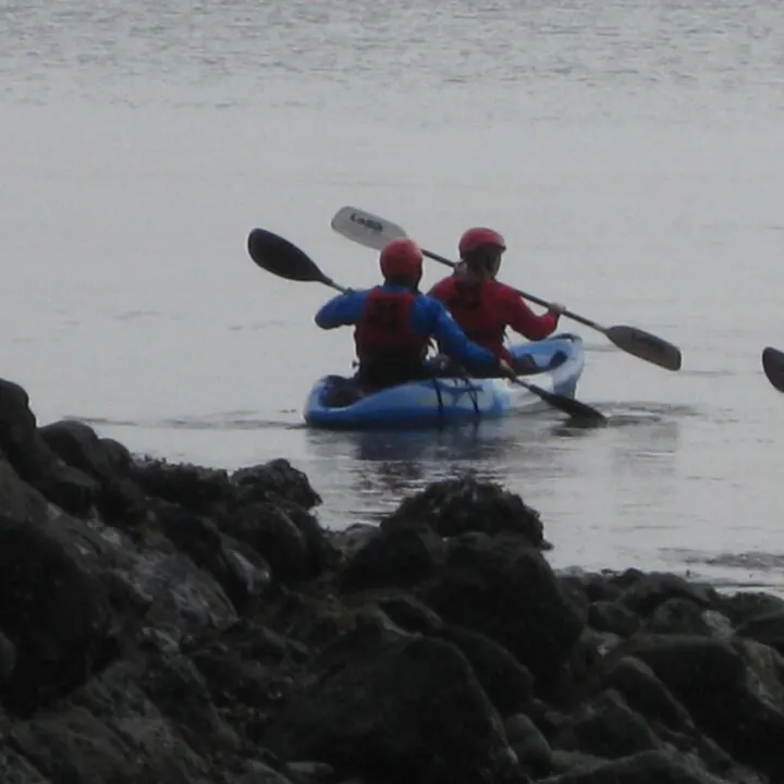 People in life jackets are kayaking and canoeing on a lake in a boat, paddle, and other watercraft for outdoor recreation and surface water sports.