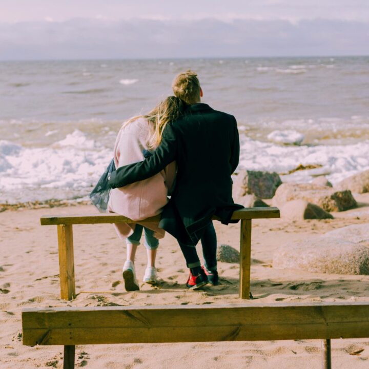Two people kiss on a bench by the ocean.