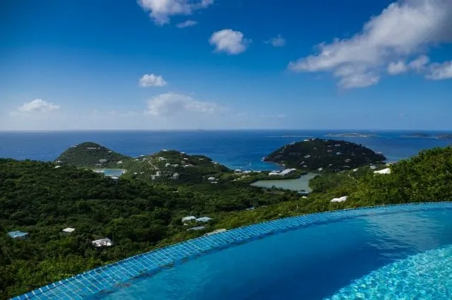 A vibrant azure sky stretches above a lush tropical landscape of trees, swimming pools, beaches, mountains, and a lagoon, creating a stunning coastal and oceanic view of the resort town.